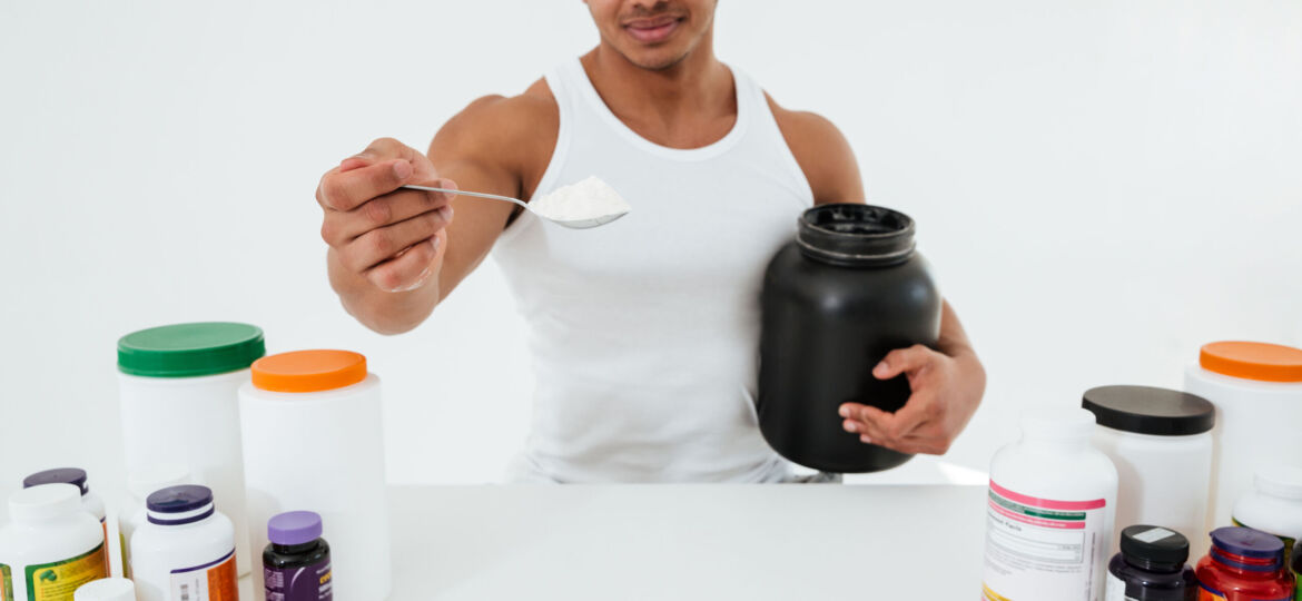 Sportsman standing over white background holding vitamins