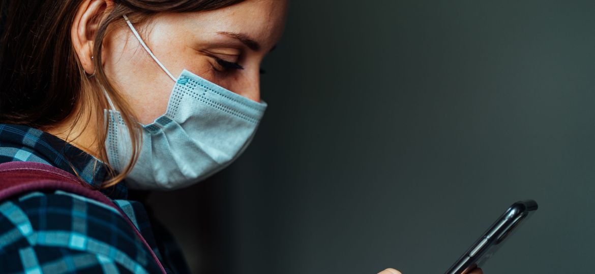 Close up of young woman in medical mask flipping news in smartphone. Portrait of adult female with mobile phone in her hands.